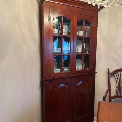 Sale Photo Thumbnail #37: Traditional cherry wooden corner cabinet featuring glass-front upper doors, solid lower panel doors, and brass H-hinges.
