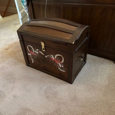 Sale Photo Thumbnail #31: Hand-painted wooden treasure chest with a domed lid, side handles, and brass latch, featuring a floral ribbon design on the front.