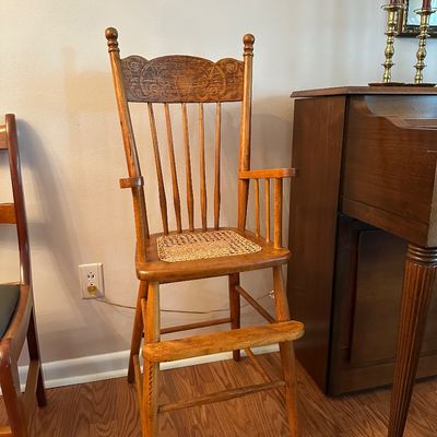 Sale Photo Thumbnail #40: Antique pressed-oak high chair with a carved crest, cane-woven seat insert, and built-in footrest.