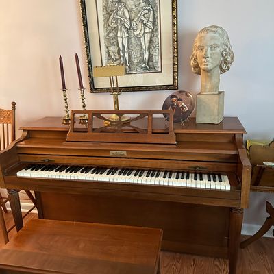 Sale Photo Thumbnail #41: Vintage Currier upright piano with matching wooden bench, accessorized with brass candlesticks, art prints, and a decorative sculpture bust.