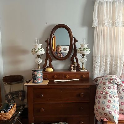Sale Photo Thumbnail #23: Antique wooden vanity dresser with a swivel oval mirror, flanked by a pair of milk glass hurricane-style table lamps with painted ivy motifs.