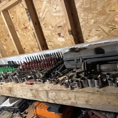 Sale Photo Thumbnail #58: Large assortment of socket wrenches and mechanic tools arranged on a wooden workbench in a shed or garage.
