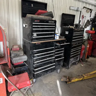 Sale Photo Thumbnail #90: Two black Craftsman rolling tool chests, stacked with top boxes and filled with drawers, in a workshop setting.