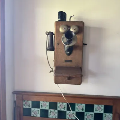 Sale Photo Thumbnail #50: Antique wall-mounted wooden hand-crank telephone featuring twin metal bells and attached earpiece receiver.
