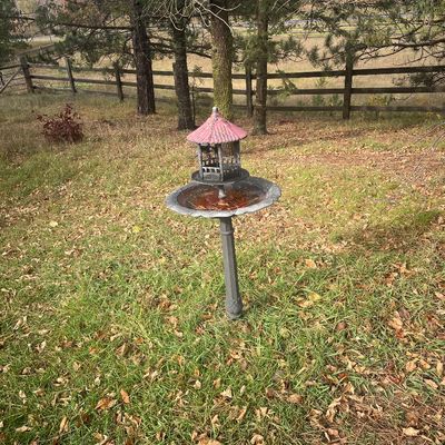 Sale Photo Thumbnail #180: Rustic cast metal bird feeder and bath combo with a pagoda-style top, featuring a weathered finish and pink roof accents.