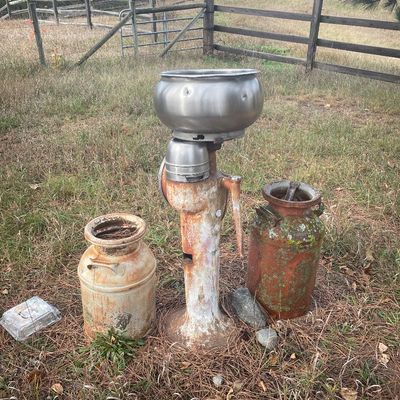 Sale Photo Thumbnail #177: Vintage cream separator with a stainless steel bowl standing outdoors, flanked by two rusted vintage metal milk cans.