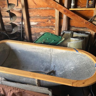 Sale Photo Thumbnail #203: Vintage galvanized metal bathtub with a natural wood top rim, set inside a workshop.