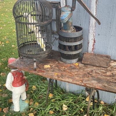 Sale Photo Thumbnail #169: Vintage iron birdcage with decorative parrot alongside a blue painted cast iron pitcher pump planter resting on a wooden stand.