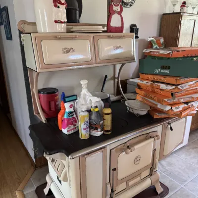 Sale Photo Thumbnail #39: Vintage Copper-Clad enamel cast iron cookstove in beige and tan, featuring a warming oven, high shelf, and various decorative kitchenware displayed on top.