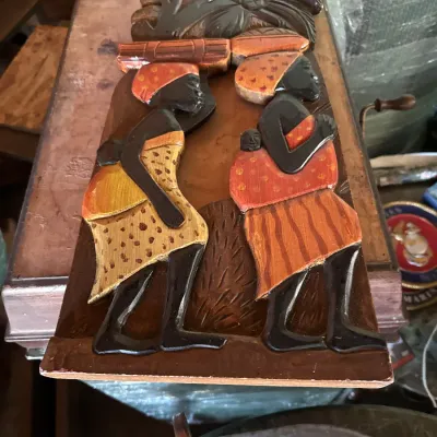Sale Photo Thumbnail #104: Hand-carved and painted wooden wall plaque depicting two women carrying goods, featuring detailed relief elements and warm earth tones.