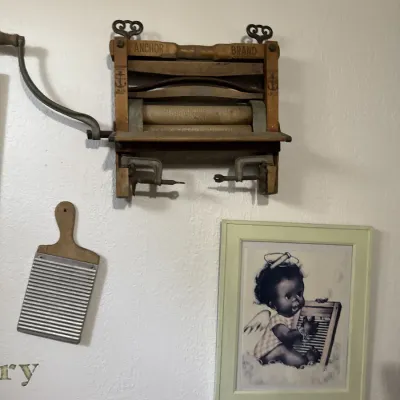 Sale Photo Thumbnail #18: Antique Anchor Brand wall-mounted hand-crank clothes wringer, paired with a vintage washboard and framed laundry-themed art.