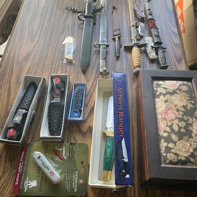 Sale Photo Thumbnail #209: Collection of military bayonets, decorative daggers, modern pocket knives, and an Airborne Ranger knife displayed alongside a wooden floral box.