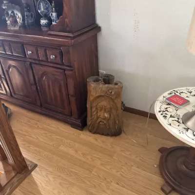 Sale Photo Thumbnail #40: Hand-carved wooden tree trunk sculpture featuring a bearded face, displayed alongside a dark wood china hutch and a floral-topped accent table.