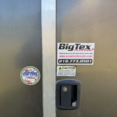 Sale Photo Thumbnail #135: Close-up view of an enclosed utility trailer door latch, featuring a Big Tex Trailers dealer decal and NATM compliance sticker.