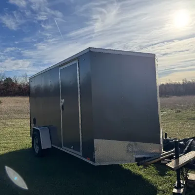 Sale Photo Thumbnail #137: Enclosed single-axle utility cargo trailer with a side access door, V-nose front, and diamond-plate gravel guard.
