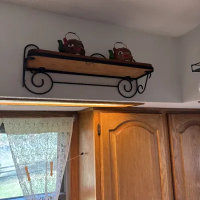 Sale Photo Thumbnail #32: Wall-mounted wood and wrought iron scrollwork shelf holding two novel ceramic teapots, positioned above wooden kitchen cabinets.
