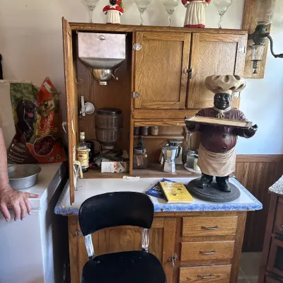 Sale Photo Thumbnail #26: Vintage oak Hoosier cabinet with built-in flour sifter and enamel work surface, displayed alongside a black chef figurine and various kitchen collectibles.