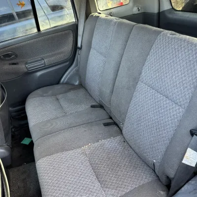 Sale Photo Thumbnail #154: Rear interior bench seat of a vehicle with gray patterned cloth upholstery, showing light wear and debris.