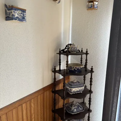 Sale Photo Thumbnail #44: Five-tier dark wood corner shelf displaying blue and white transferware porcelain, accompanied by matching wall-mounted ceramic accessories.