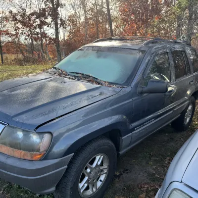 Sale Photo Thumbnail #152: Dark gray Jeep Grand Cherokee Laredo SUV parked outdoors, featuring roof rails and window rain guards.
