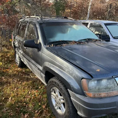 Sale Photo Thumbnail #151: Dark gray Jeep Grand Cherokee Laredo SUV, late 1990s or early 2000s model, parked outdoors with visible roof rack and alloy wheels.