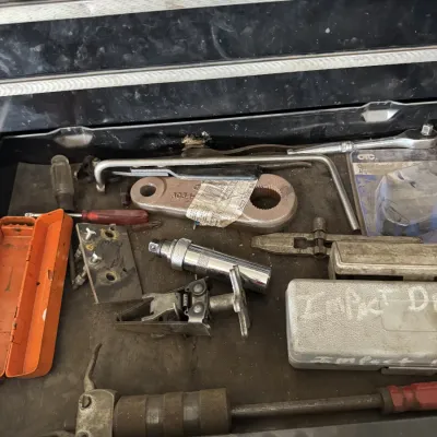 Sale Photo Thumbnail #79: Assorted specialty automotive tools and hardware stored inside a metal toolbox drawer, including a heavy-duty pitman arm, impact driver case, and various hand tools.