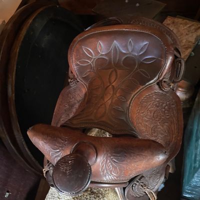 Sale Photo Thumbnail #195: Vintage brown leather Western saddle featuring intricate hand-tooled floral patterns and decorative stitching on the seat.