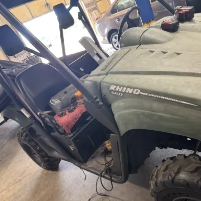Sale Photo Thumbnail #98: Yamaha Rhino 660 side-by-side utility vehicle in olive green, featuring a roll cage, off-road tires, and bucket seating.
