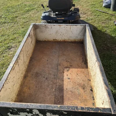 Sale Photo Thumbnail #119: Heavy-duty metal utility tow-behind yard cart, showing significant surface rust and paint wear, attached to a Poulan Pro riding lawn mower.