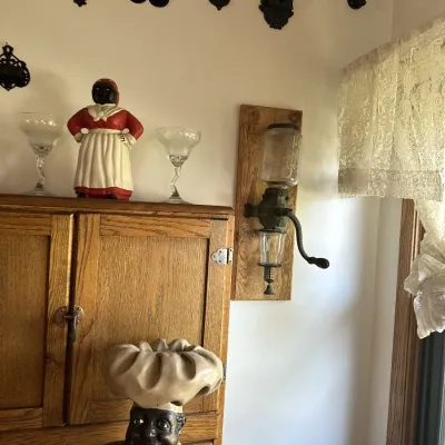 Sale Photo Thumbnail #23: Vintage kitchen decor display including a wall-mounted Arcade coffee grinder, Black Americana figurines, cast iron wall trivets, and an oak cabinet.