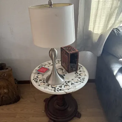 Sale Photo Thumbnail #41: Brushed nickel table lamp resting on a round marble-top end table with floral inlay and a carved dark wood base.