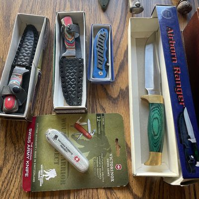 Sale Photo Thumbnail #207: Collection of collectible knives in original boxes, including an Airborn Ranger fixed-blade knife with a green handle and a Victorinox Wounded Warrior Project Swiss Army knife in blister packaging.