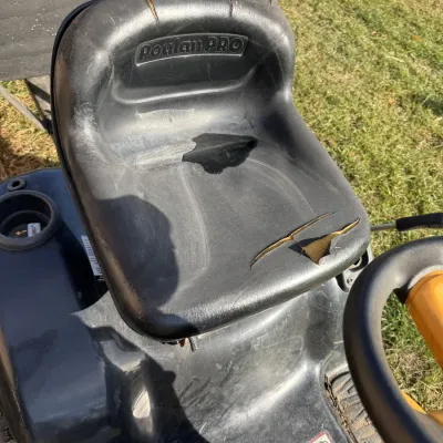 Sale Photo Thumbnail #121: Black Poulan PRO riding lawn mower seat featuring noticeable tears in the vinyl upholstery exposing the underlying foam.