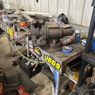 Sale Photo Thumbnail #60: Heavy-duty cast iron bench vise mounted on a metal workshop workbench alongside various automotive and hardware supplies.