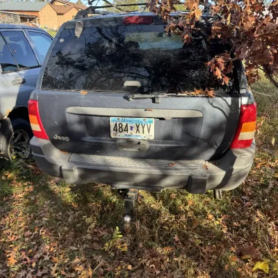 Sale Photo Thumbnail #148: Rear view of a dark grey Jeep Grand Cherokee SUV with Minnesota license plates, equipped with a trailer hitch receiver and ball.