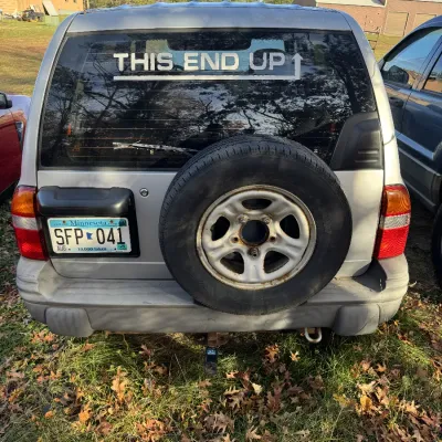 Sale Photo Thumbnail #159: Rear view of a silver compact SUV with a rear-mounted spare tire and a white "THIS END UP" decal on the back window.