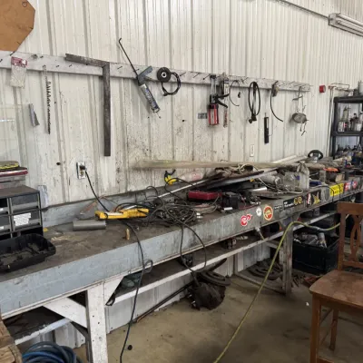 Sale Photo Thumbnail #64: Workshop workbench area featuring an assortment of hand tools, hardware organizers, automotive supplies, and a wooden chair.