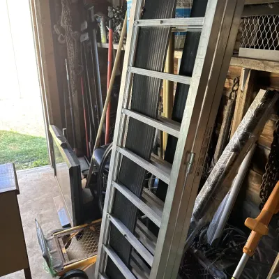 Sale Photo Thumbnail #109: Aluminum folding loading ramp resting upright in a workshop alongside various lawn tools and hardware.