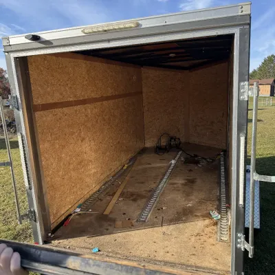 Sale Photo Thumbnail #133: Interior view of an enclosed cargo trailer featuring wood paneling, floor tie-down tracks, and a fold-down rear door.