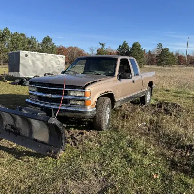 Sale Photo Thumbnail #129: Tan Chevrolet extended-cab pickup truck equipped with a front snowplow attachment, showing visible body rust around the wheel wells.