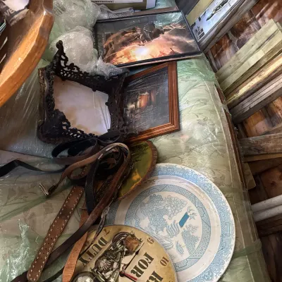 Sale Photo Thumbnail #145: Collection of assorted household items including a motorcycle-themed wall clock, blue and white transferware platter, leather belts, framed artwork, and a vintage canister vacuum.