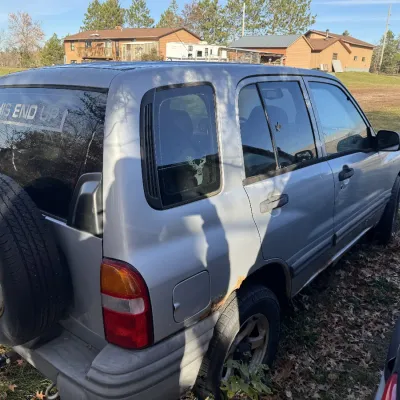 Sale Photo Thumbnail #160: Silver Suzuki Grand Vitara SUV with rear-mounted spare tire, showing visible rust and exterior wear.