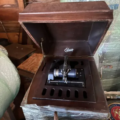 Sale Photo Thumbnail #103: Antique Edison cylinder phonograph housed in a dark wooden cabinet with an open lid, featuring a hand-crank handle on the side.