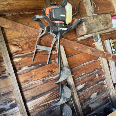 Sale Photo Thumbnail #146: Strikemaster gas-powered ice auger with dual handles, stored inside a wooden shed.