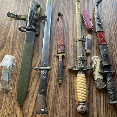 Sale Photo Thumbnail #208: Collection of vintage military bayonets, ornamental daggers, and pocket knives displayed on a wooden surface.