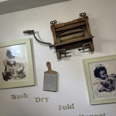 Sale Photo Thumbnail #17: Vintage Anchor Brand hand-crank clothes wringer wall display paired with a small washboard and two framed laundry-themed art prints.