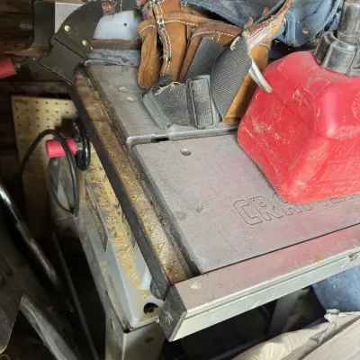Sale Photo Thumbnail #116: Vintage Craftsman table saw showing wear and sawdust, topped with leather tool belts and a red plastic gas can.