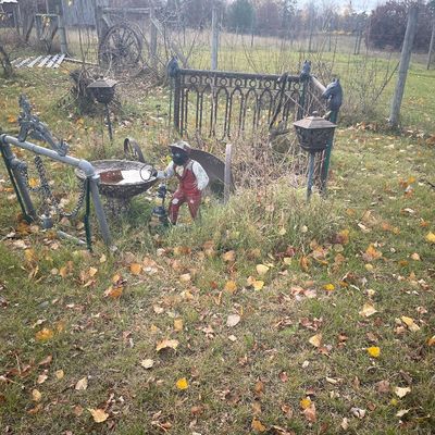 Sale Photo Thumbnail #174: Assorted vintage garden decor including a cast iron lawn jockey statue, bird bath, decorative metal fence panel, and solar yard lights set in a grassy yard.