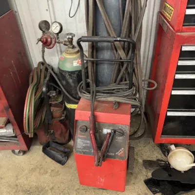 Sale Photo Thumbnail #69: Vintage Snap-on Super 550 battery charger and booster on a rolling cart, shown alongside compressed gas cylinders and welding equipment in a workshop.