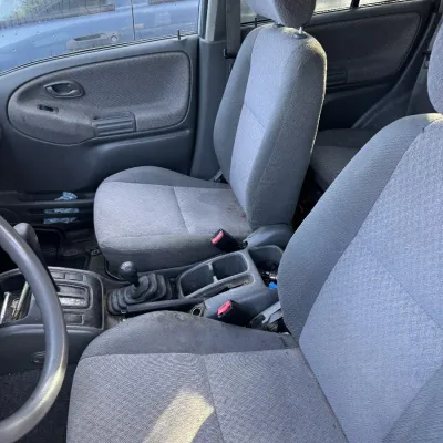 Sale Photo Thumbnail #156: Interior view of an older vehicle featuring grey cloth bucket seats, manual transmission shift lever, and center console.